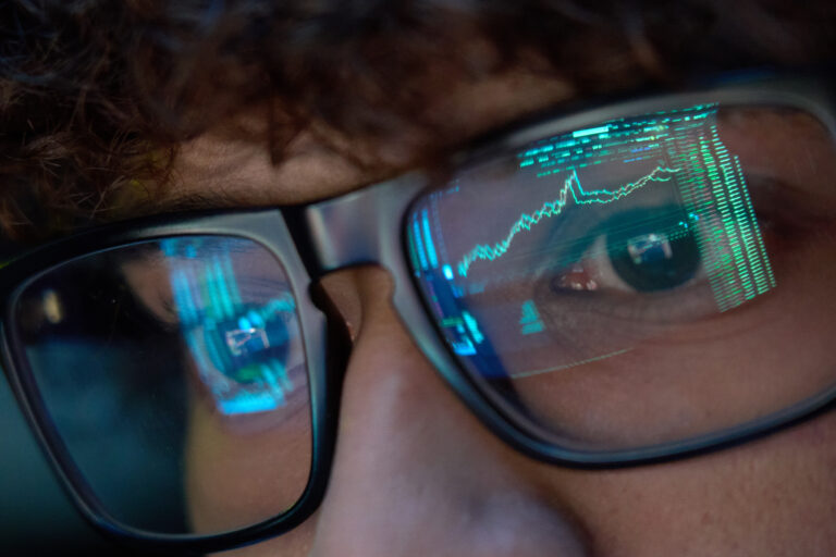 person looking at trading charts reflecting in glasses