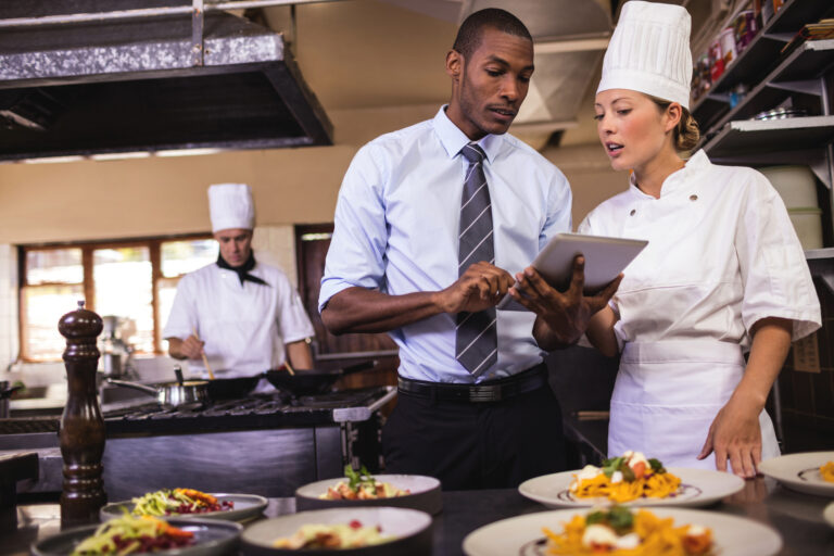 restaurant workers prepare food while holding tablet device