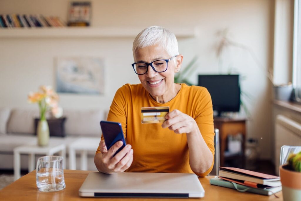 Mature woman smiling while holding credit card and phone fhyNEdl