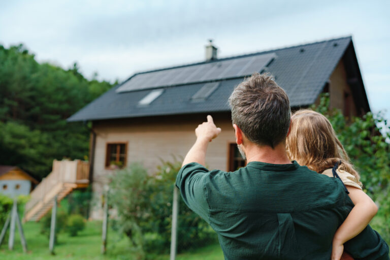 adult with child in arms pointing to a house with solar panels on its roof