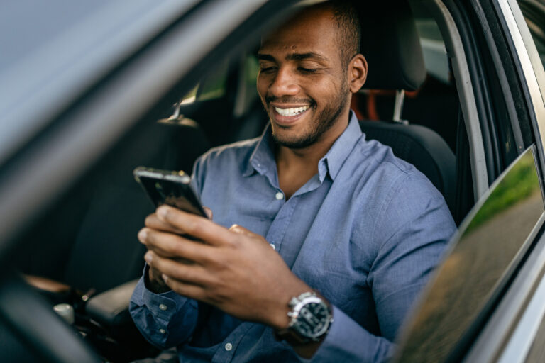 person in car smiling while gazing at a smartphone