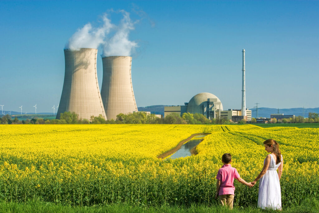 mother and son hold hands in a field of flowers outside a nuclear power station