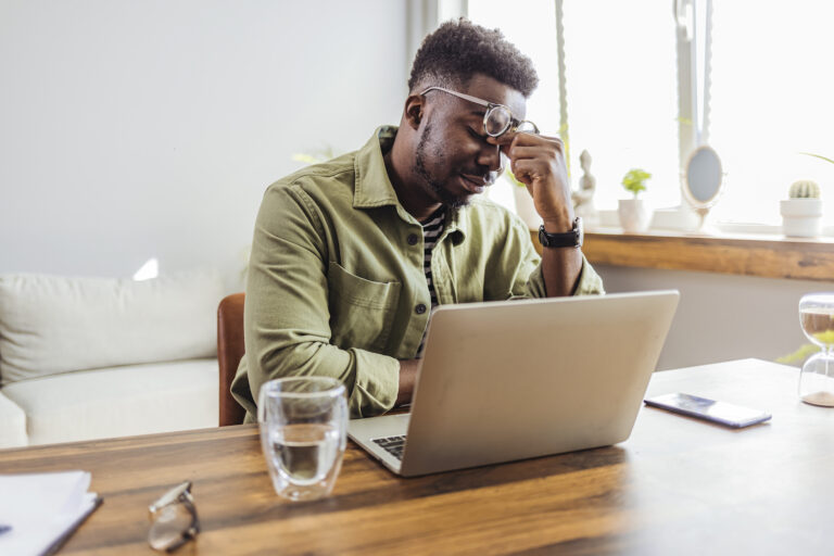 man rubs eyes in frustration and fatigue in front of laptop