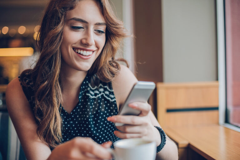 person holding a smartphone and a mug