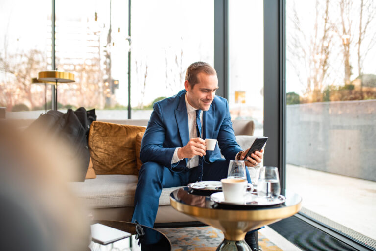investor looks at phone in cafe while drinking espresso
